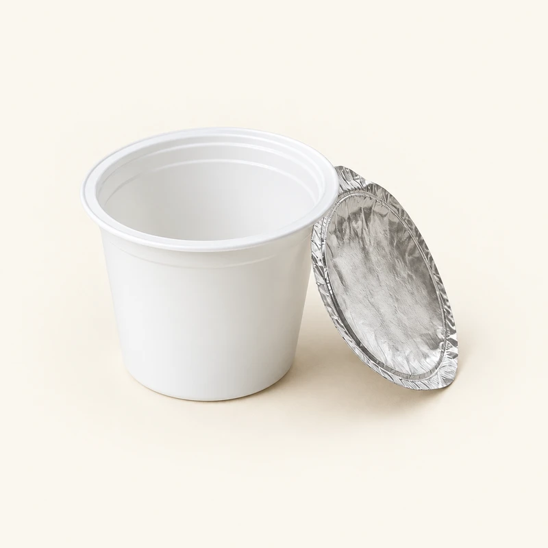 Leerer weißer Kunststoffbecher mit vollständig abgezogenem Aludeckel daneben.